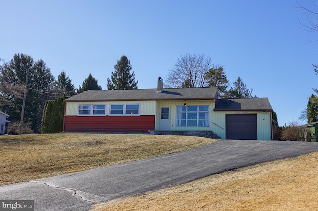 single story home with aphalt driveway, an attached garage, a chimney, and a front lawn