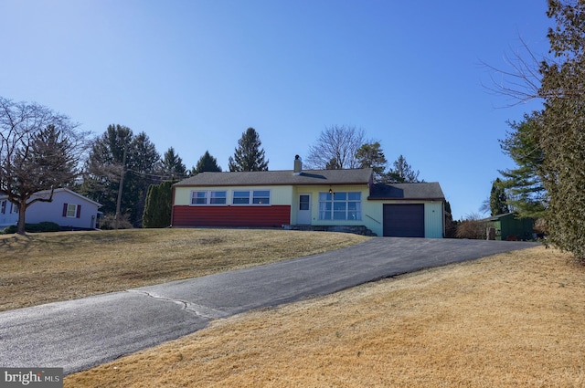 single story home featuring a garage, a front lawn, a chimney, and driveway