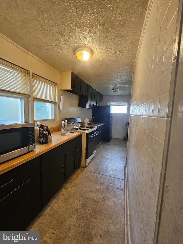 2916 Woodland Ave, Baltimore, MD 21215 - kitchen featuring dark cabinetry, light countertops, a textured ceiling, range with gas cooktop, and stainless steel microwave