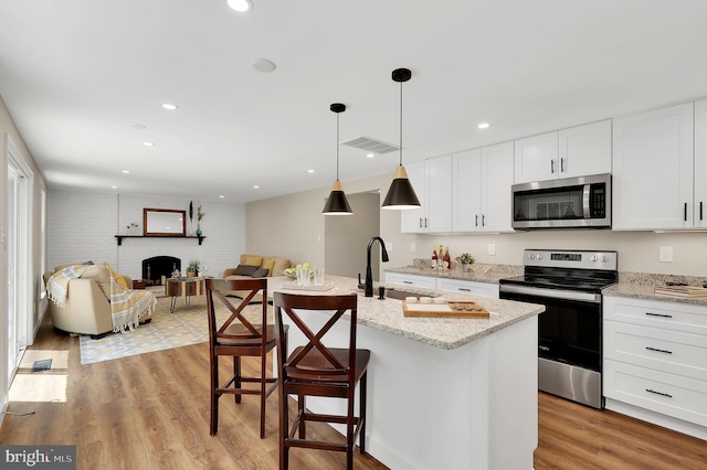 kitchen with light wood-style flooring, a sink, appliances with stainless steel finishes, white cabinetry, and open floor plan