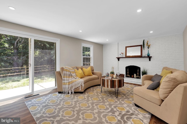 living room with visible vents, wood finished floors, recessed lighting, brick wall, and a fireplace