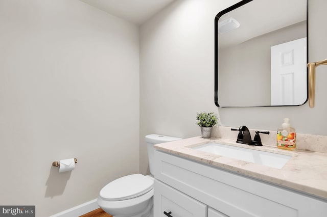 half bathroom featuring toilet, vanity, and baseboards