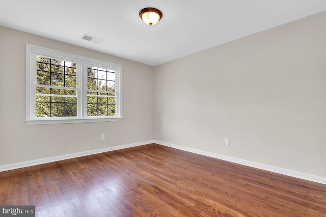 empty room with wood finished floors, baseboards, and visible vents