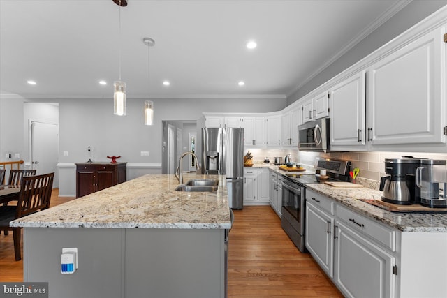 kitchen featuring crown molding, an island with sink, decorative backsplash, appliances with stainless steel finishes, and light wood-style floors