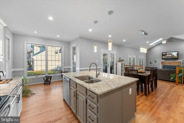 kitchen featuring a brick fireplace, a center island with sink, light wood-style flooring, appliances with stainless steel finishes, and a sink