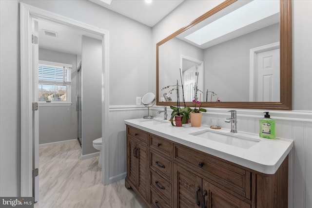 bathroom featuring wainscoting, a skylight, marble finish floor, and a sink