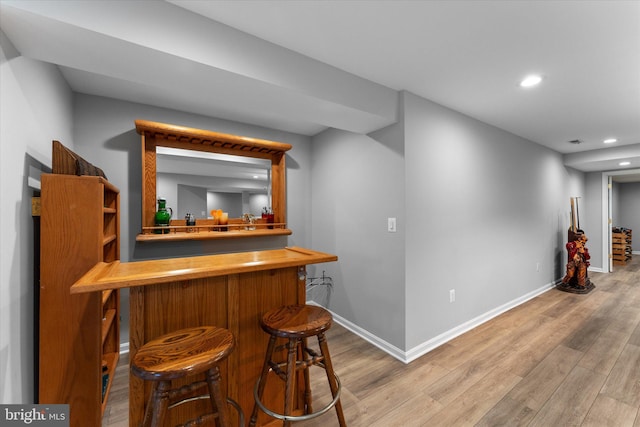 bar with light wood-style flooring, a bar, and baseboards