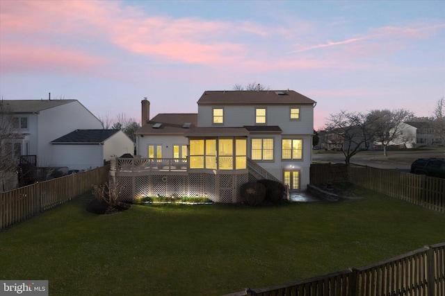 back of property at dusk with a yard, a deck, a chimney, and a fenced backyard