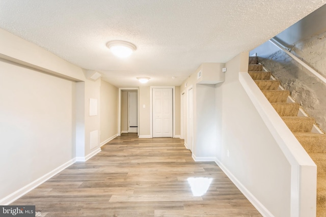 interior space with stairway, baseboards, a textured ceiling, and wood finished floors