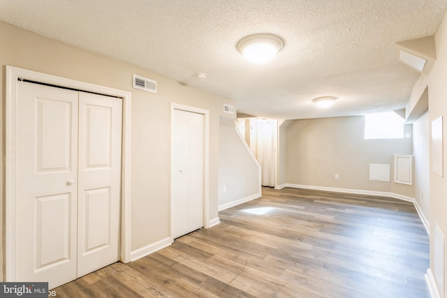 below grade area with visible vents, baseboards, a textured ceiling, and wood finished floors