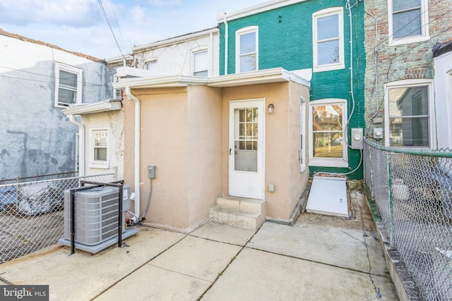 doorway to property featuring stucco siding, central AC unit, and fence