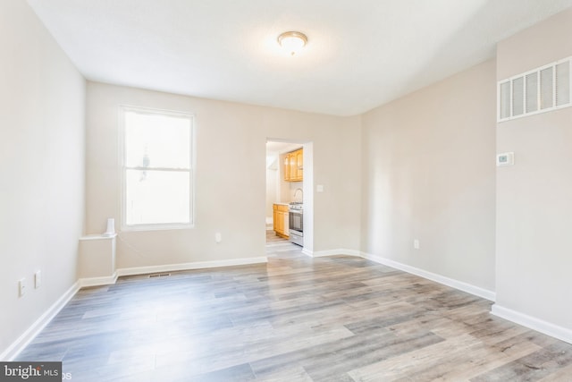 spare room with light wood-style floors, visible vents, and baseboards