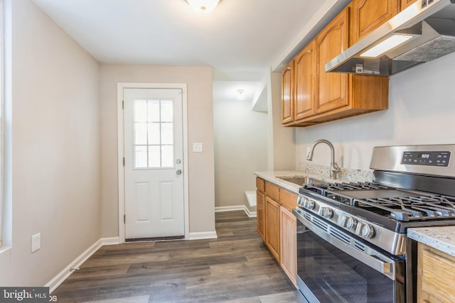 kitchen with light stone counters, dark wood-style flooring, a sink, under cabinet range hood, and stainless steel gas stove