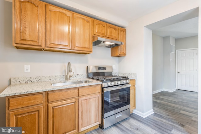 kitchen featuring light stone countertops, gas stove, light wood-style flooring, a sink, and under cabinet range hood