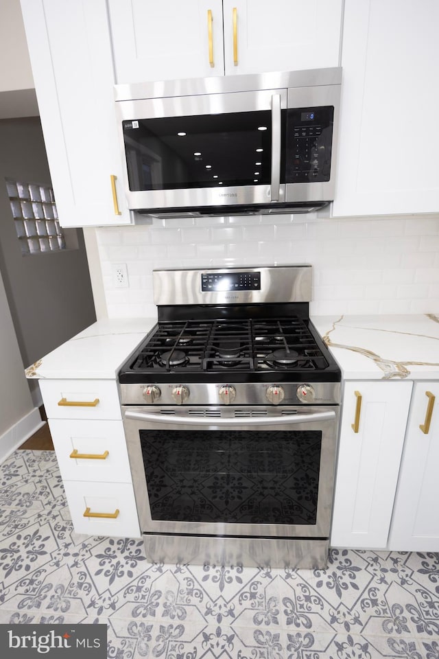 kitchen featuring light stone counters, tasteful backsplash, stainless steel appliances, white cabinets, and tile patterned flooring