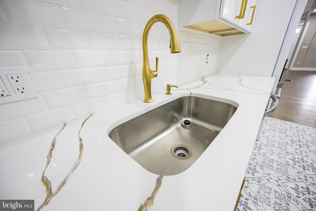 interior details with decorative backsplash, light stone counters, wood finished floors, and a sink