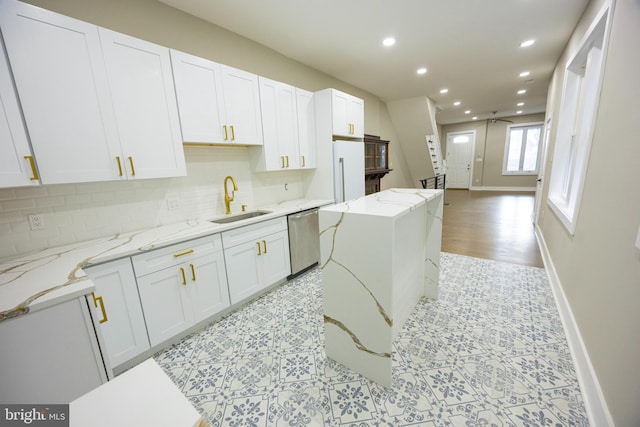 kitchen featuring a kitchen island, a sink, white cabinets, stainless steel dishwasher, and tasteful backsplash