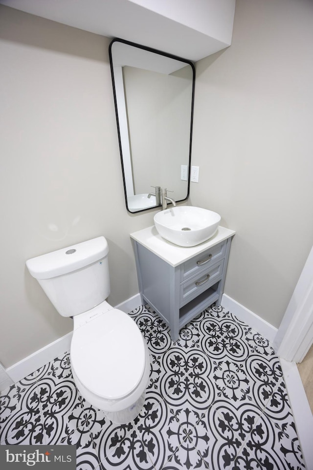 half bath with tile patterned flooring, toilet, vanity, and baseboards