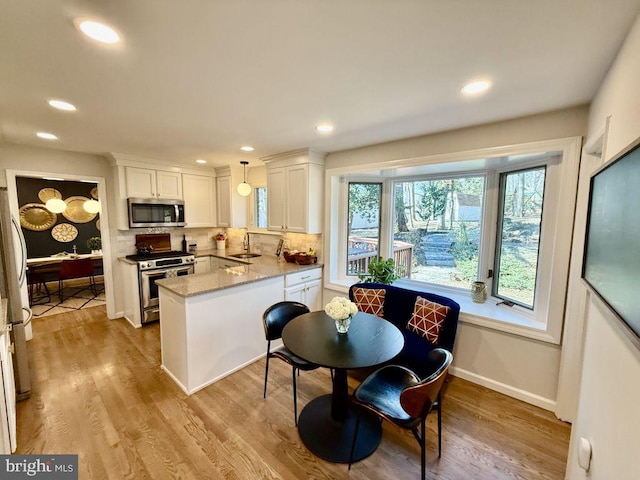 kitchen featuring a peninsula, a sink, decorative backsplash, white cabinets, and appliances with stainless steel finishes