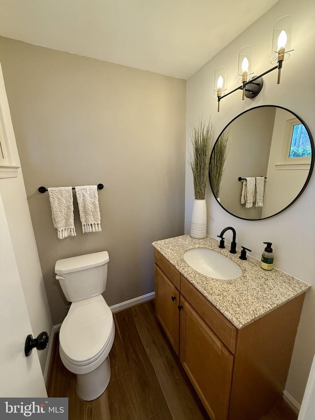 bathroom featuring baseboards, toilet, wood finished floors, and vanity