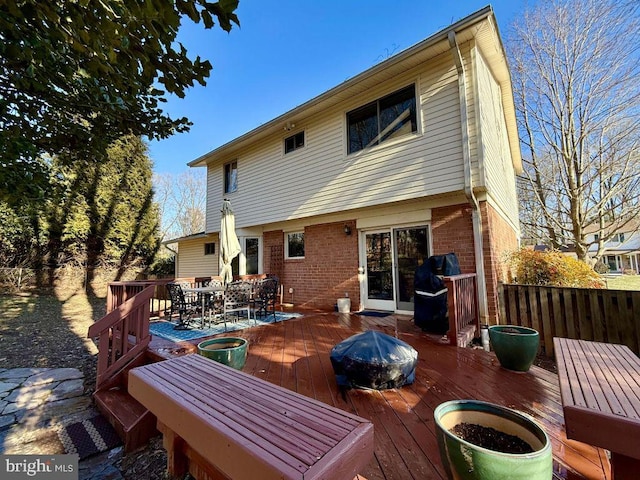 rear view of house featuring a deck, outdoor dining area, a fire pit, and brick siding