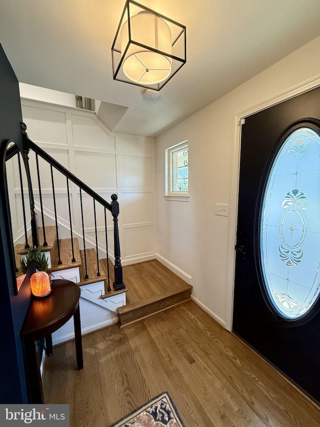 entrance foyer featuring visible vents, wood finished floors, stairway, a decorative wall, and baseboards