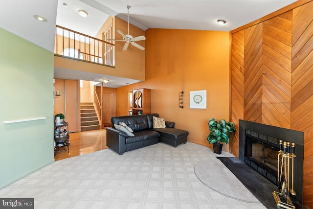 living area featuring stairs, carpet flooring, a fireplace, high vaulted ceiling, and a ceiling fan