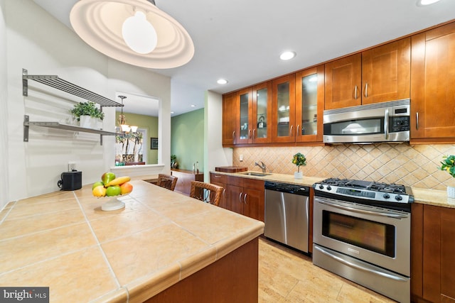 kitchen featuring a sink, tasteful backsplash, appliances with stainless steel finishes, brown cabinetry, and glass insert cabinets