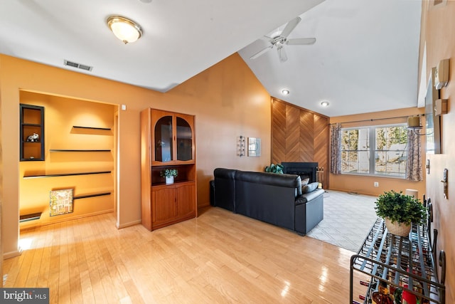 living room with visible vents, ceiling fan, vaulted ceiling, light wood-style flooring, and a fireplace