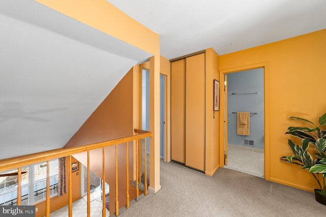 hallway featuring baseboards, an upstairs landing, visible vents, and light carpet