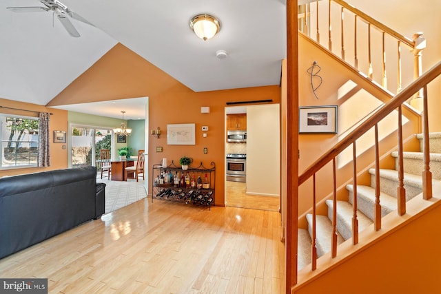 foyer with ceiling fan with notable chandelier, vaulted ceiling, stairway, and light wood-style floors