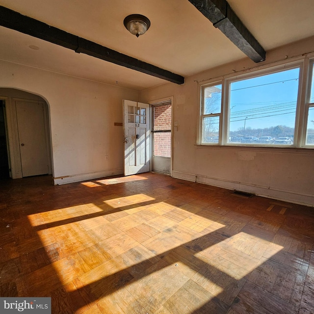 spare room with beamed ceiling, visible vents, arched walkways, and baseboards