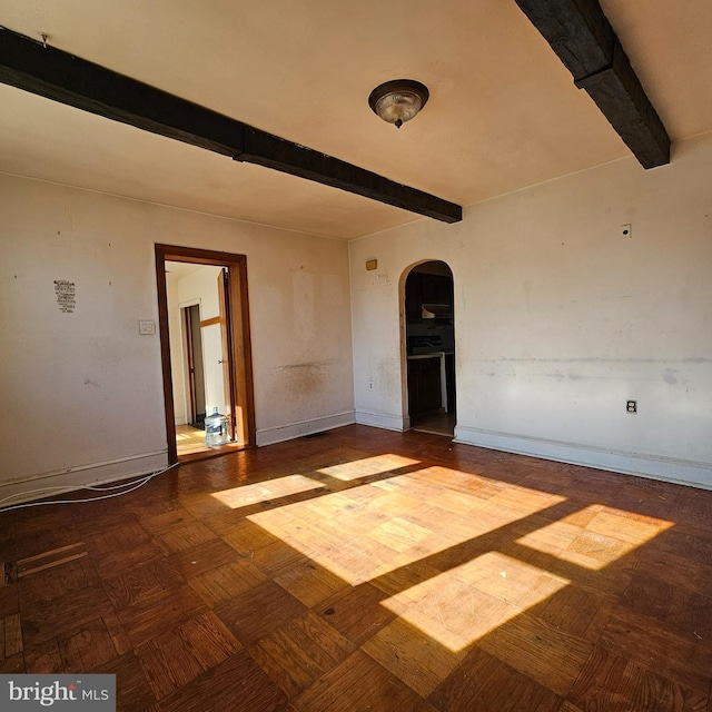 empty room featuring beamed ceiling, arched walkways, and baseboards