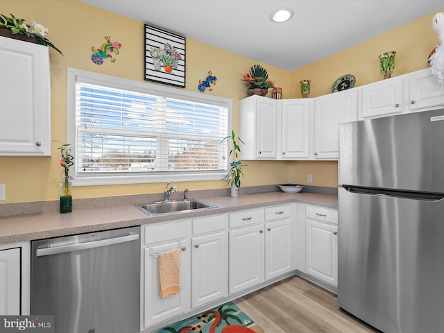 kitchen with a sink, light countertops, white cabinets, appliances with stainless steel finishes, and light wood-type flooring