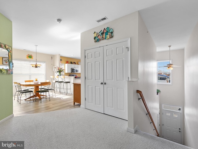 interior space featuring an upstairs landing, visible vents, light carpet, and baseboards