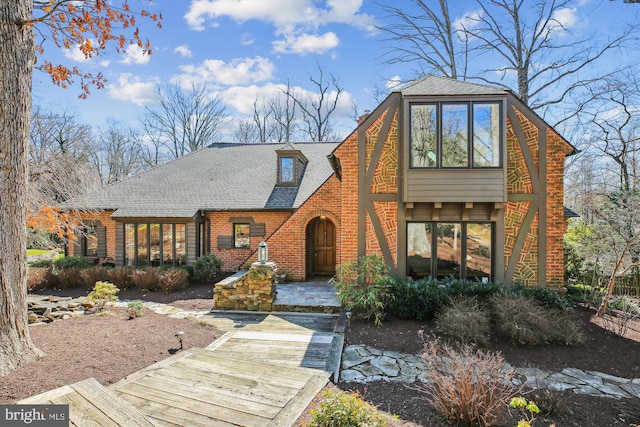 view of front of property featuring brick siding and roof with shingles