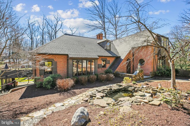 view of front of house featuring brick siding, a chimney, and a shingled roof