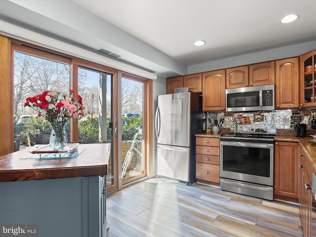 kitchen featuring decorative backsplash, glass insert cabinets, brown cabinets, and appliances with stainless steel finishes