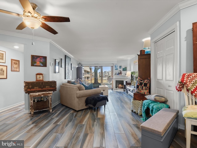 living room featuring crown molding, ceiling fan, baseboards, a lit fireplace, and wood finished floors