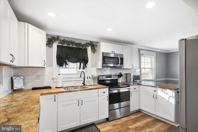 kitchen with ornamental molding, a sink, wood finished floors, white cabinetry, and stainless steel appliances