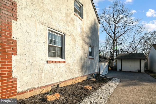 view of side of home featuring stucco siding, an outbuilding, driveway, a detached garage, and brick siding