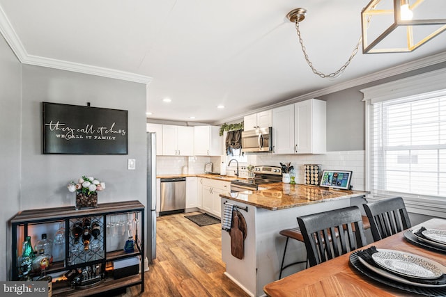 kitchen with a sink, a peninsula, ornamental molding, and stainless steel appliances