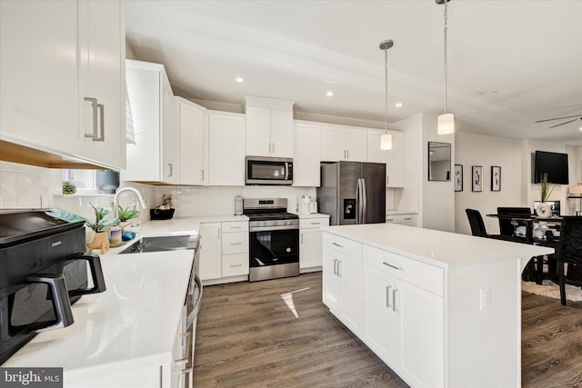 kitchen with a sink, a kitchen island, light countertops, appliances with stainless steel finishes, and dark wood-style flooring