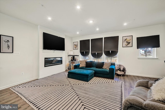 living room with a glass covered fireplace, recessed lighting, wood finished floors, and baseboards