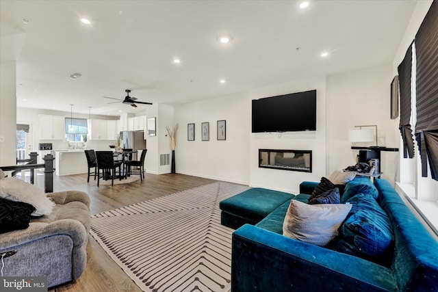 living area with wood finished floors, visible vents, a ceiling fan, recessed lighting, and a glass covered fireplace