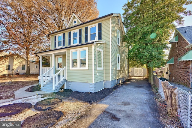 traditional style home featuring an outbuilding, covered porch, aphalt driveway, and fence