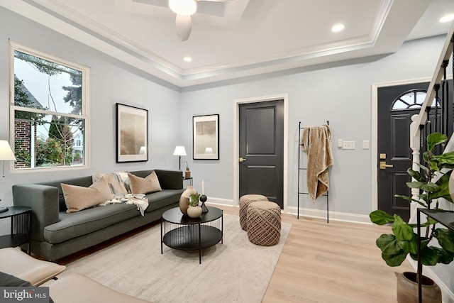 living area with a tray ceiling, baseboards, light wood-style flooring, and crown molding