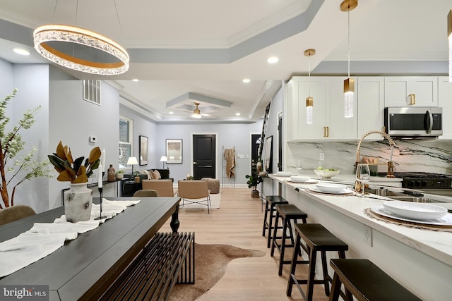 kitchen featuring visible vents, ornamental molding, white cabinets, stainless steel microwave, and a raised ceiling