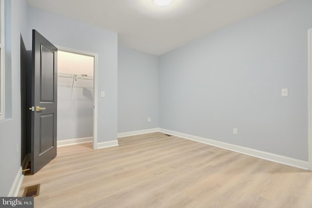 unfurnished bedroom with baseboards, visible vents, light wood-style flooring, a spacious closet, and a closet