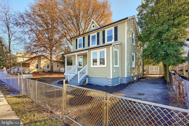 traditional style home featuring covered porch, an outdoor structure, a storage unit, a fenced front yard, and aphalt driveway